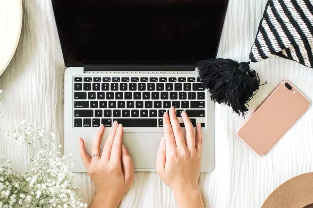 Mains tapant sur un ordinateur portable, téléphone à côté sur un bureau