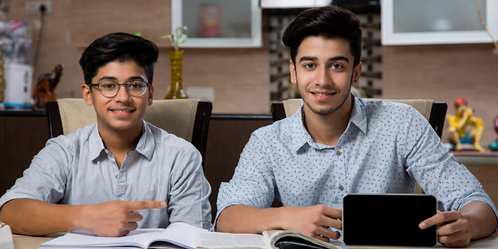 Deux étudiants travaillant sur leur mémoire de comptabilité avec des livres ouverts et une tablette.