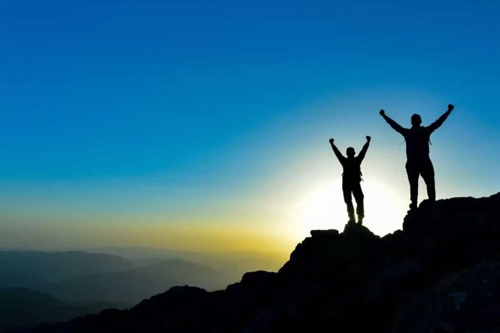 Deux randonneurs au sommet d’une montagne au lever du soleil, symbole de la réussite d’un mémoire de littérature