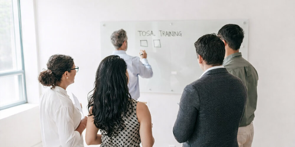 Formateur animant une session de formation professionnelle devant un tableau blanc avec des collaborateurs en entreprise.