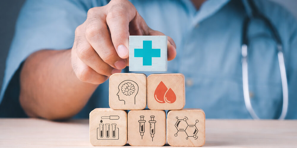 Professionnel de santé plaçant un cube avec une croix médicale sur une pyramide de blocs illustrant les domaines du soin