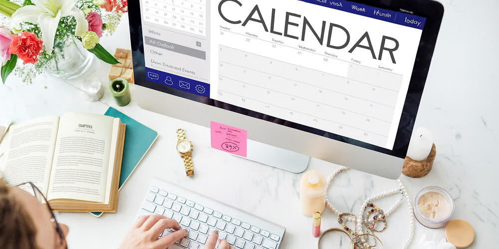 Étudiante organisant son planning de rédaction sur un ordinateur avec un calendrier, entourée de livres et d’outils de travail sur un bureau lumineux.