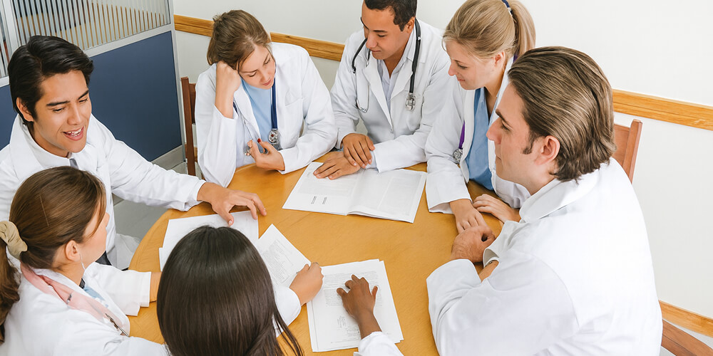Groupe de professionnels de santé en réunion autour d’une table, discutant de documents médicaux pour collaborer sur un projet ou un mémoire.
