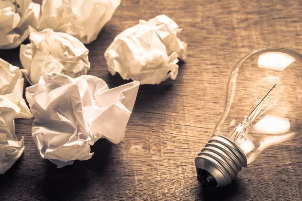 Papier froissé et ampoule sur un bureau, illustration des erreurs à éviter lors d’une soutenance de mémoire