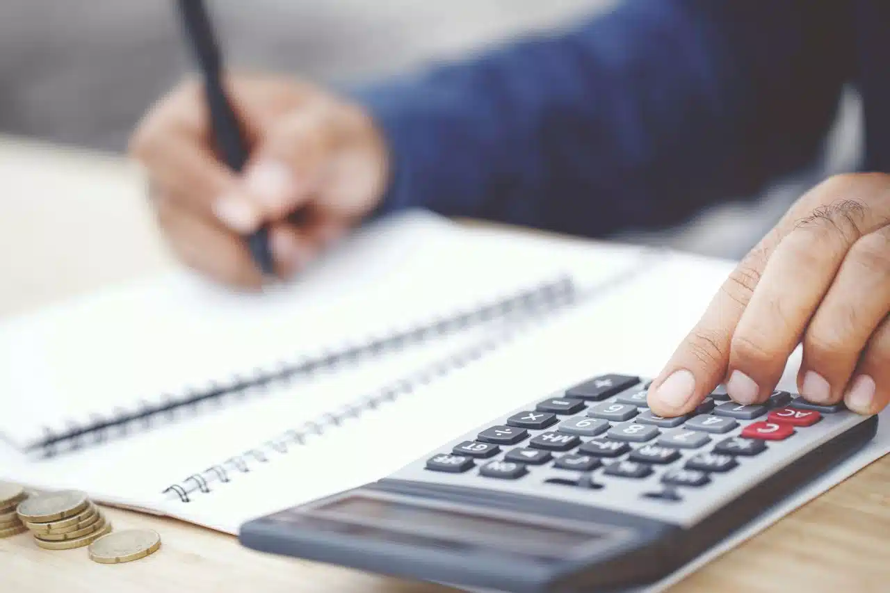 Aide à la rédaction de mémoire DSCG par nos rédacteurs spécialisés Étudiant rédigeant au stylo dans un cahier, calculatrice à la main, illustrant la rédaction d'un mémoire DSCG
