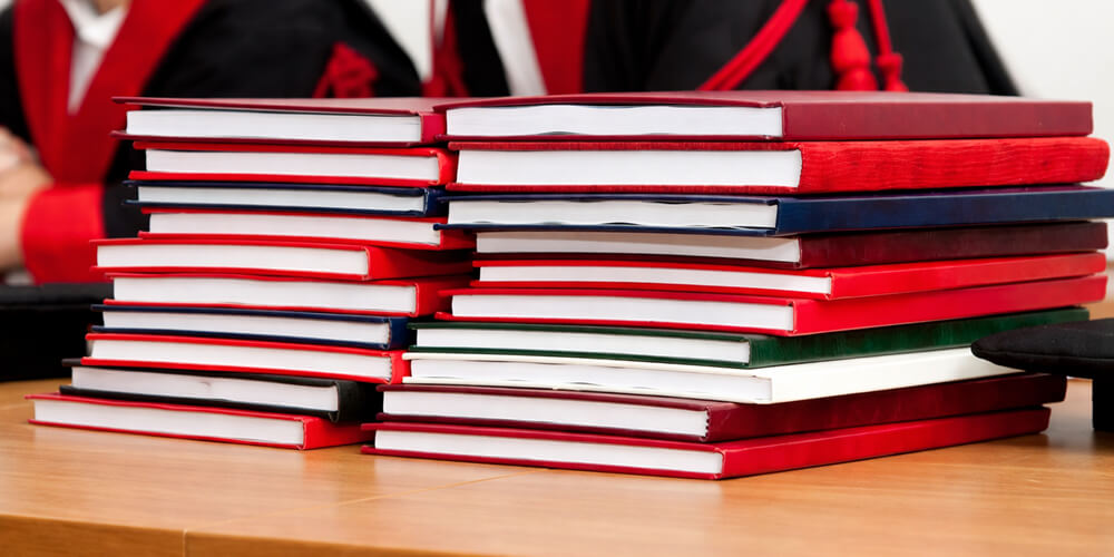 Pile de mémoires reliés posés sur une table, avec jury universitaire en arrière-plan