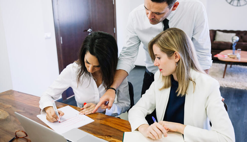 Trois collègues en réunion analysant un document sur un bureau, illustrant le travail collaboratif d’analyse scientifique.