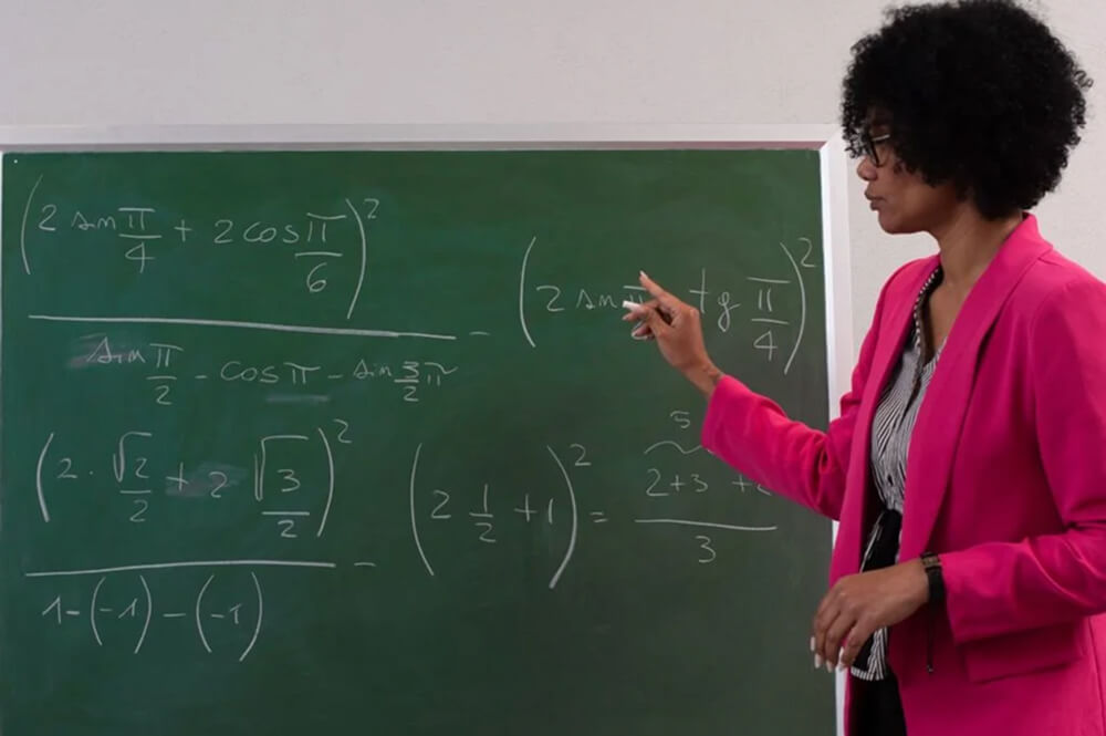 Enseignante expliquant des formules mathématiques complexes au tableau vert pendant un cours universitaire.